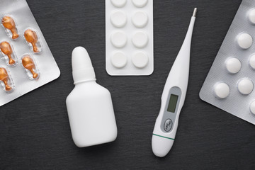 Thermometer, nasal drops and tablets on dark slate board. Flat lay. Meds for flue treatment, health...