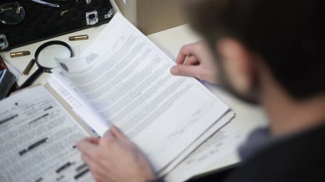 Detective searching paper with fingerprints among reports and other documents