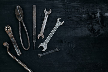 Old, rusty tools lying on a black wooden table. Hammer, chisel, metal scissors, wrench.