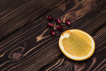 Orange and pomegranate slices on a dark wooden background. Place for your text