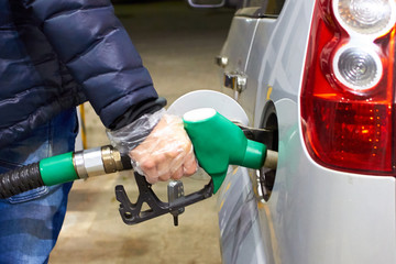 man in a disposable glove runs the car with gasoline at self-service gas station  in the evening. Personal hygiene in public places. Green color of a petrol gun as a sign of environmental friendliness