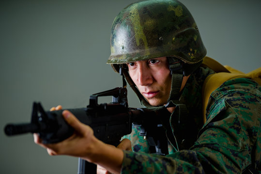 Portrait of young soldier holding in his hands a rifle, wearing a military uniform, in a gray background