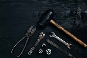 Old, rusty tools lying on a black wooden table. Hammer, chisel, metal scissors, wrench.