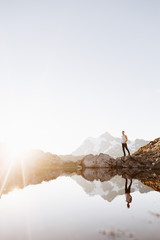 man reflects in mountain lake with peak at sunrise