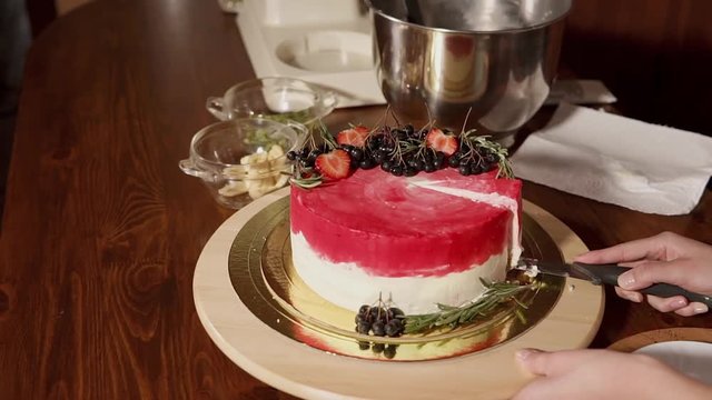close up shot of the sweet cake, which is decorated with strawberries and berries, a woman cuts a piece of dessert with a knife and puts it on a plate, the food stands on the table