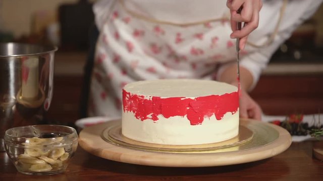 Close look at the pasrty chef smearing cream on the cake at home. She is applying pink berry cream.