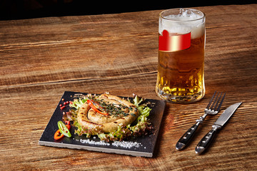 Fototapeta na wymiar Homemade sausage with garlic and spices on a slate plate, a glass of beer behind of plate on wooden table