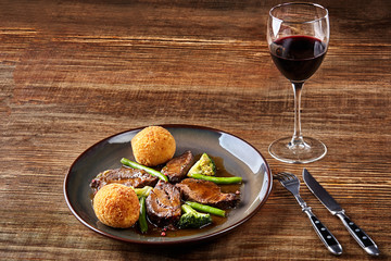 Stewed beef with vegetables and a glass of red dry wine on wooden table, close up. Hot Meat Dishes.