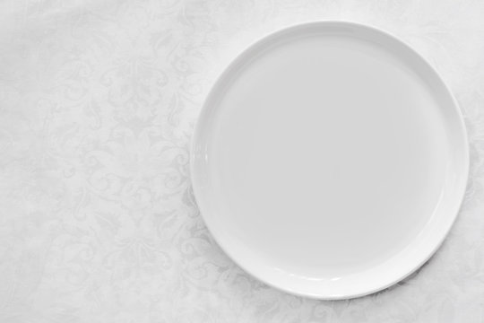 Empty White Plate over Brocade Tablecloth Top View