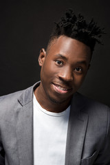 Close-up portrait of handsome black man with charming smile. Studio shot of well-dressed african guy wears white T-shirt and gray jacket.