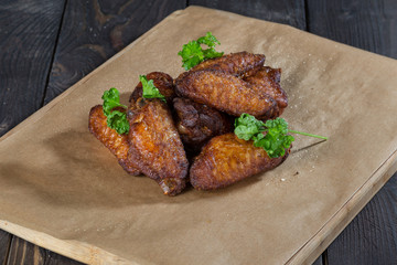 Fried chicken wings/ delicious fast food. Fried chicken wings with a grill on brown paper on a wooden table with green sprigs.