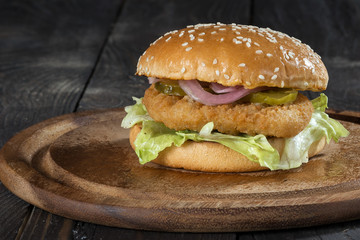 Hamburger with chiken cutlet/ Hamburger  bun with sesame and chicken cutlet on a wooden board close-up.