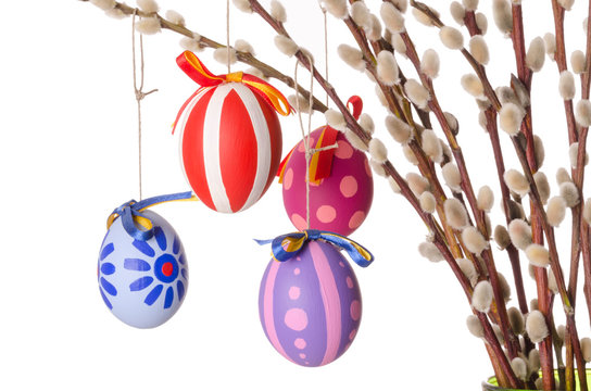Easter eggs on willow bouquet with catkins, horizontal. Four hand-painted colored Paschal eggs on branches of sallows or also called osiers, with aments. Photo on white background.