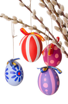 Easter eggs on willow bouquet with catkins, vertical. Four hand-painted colored Paschal eggs on branches of sallows or also called osiers, with aments. Photo on white background.