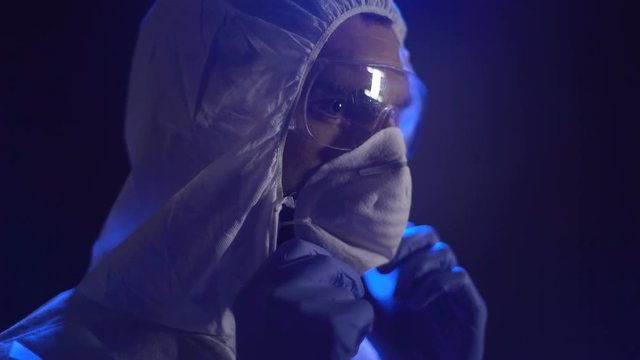 Chemist in lab costume wearing mask, secret manufacture of biological weapons