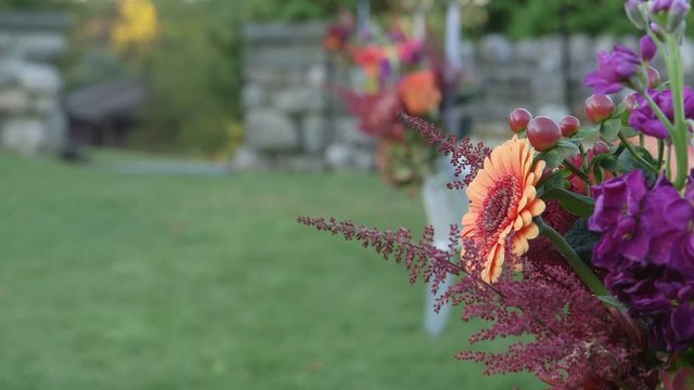 Rack focus on purple and orange flower arrangement set up for outdoor wedding.