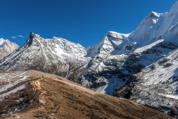 Mountain range and snow peak with traveler group along trail path in autumn season in clear blue sky day at Yading National Park,  Daocheng, Sichuan, China