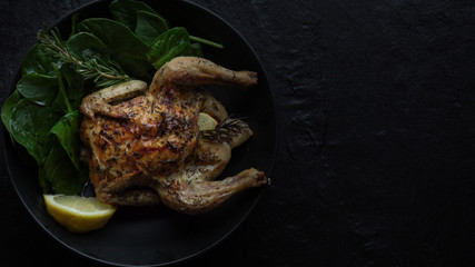 Broiled Cornish Game Hen with Spinach on Black Background.