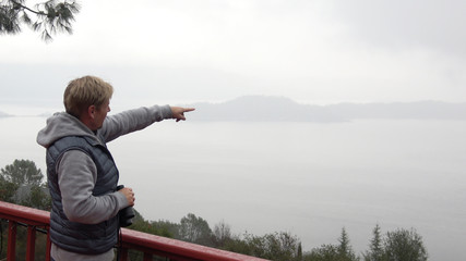 Man overlooking a foggy misty lake is pointing towards the landscape.