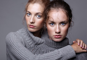 Two young women in gray sweaters on grey background. Beautiful girls stretching hands forward in embrace. Female friendship concept