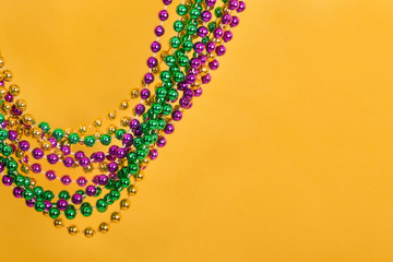 Mardi Gras beads against golden yellow background with copy space