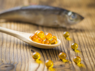Bright wooden spoon with capsules of fish oil on the background of the fish. Selective focus.