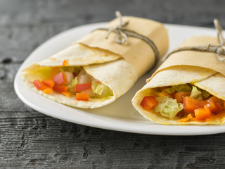Two vegetable roll tortilla from wheat flour in white bowl on a black table.