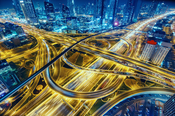 Naklejka premium Widok z lotu ptaka na duże skrzyżowanie autostrad z ruchem w Dubaju, Zjednoczone Emiraty Arabskie, w nocy. Malowniczy pejzaż. Kolorowe tło transportu, komunikacji i jazdy.