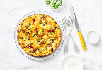 Potatoes and vegetables tortilla on a light background, top view. Potatoes, green beans, bell peppers, green peas, cheese, eggs casserole - a delicious breakfast or snack