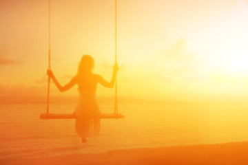Woman on swing silhouette with brightly sunset colors on background