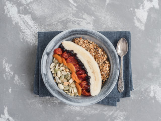 Muesli with banana, blueberries, dried apricots, carnelian cherry, peanuts and pumpkin seeds, in an old plate on a gray table