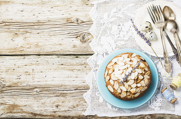 Simple homemade pecan pie decorated with petals of almond with a wooden background Serving Easter used blue and yellow colors, quail eggs, lavender flowers, vintage linen tablecloth handmade.