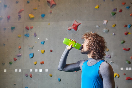Active guy drinking water from plastic bottle on background of climbing wall