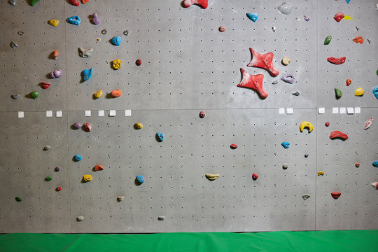 Climbing wall with colorful grips and green mat near by