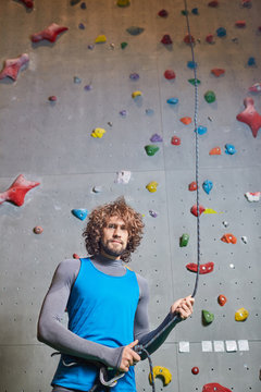 Attractive young man with curly hair holding by rope for climbing before training