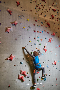 Contemporary man in activewear hanging on rope while climbing wall at leisure