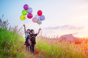 boy and girl kids playing around at the meadow on the hills with holding in hand multicolor ballons