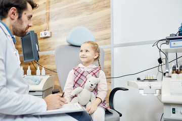 Happy adorable child with toy talking to doctor and listening to his advice