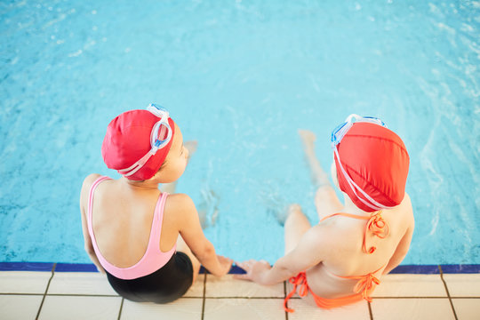 Overview of two girlfriends in swimwear spending time by swimming-pool after school