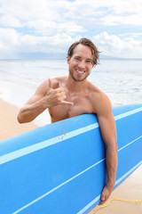 Surf beach active sport lifestyle. Happy surfer man holding surfboard doing shaka hand sign having fun in Hawaii ocean. Watersport living.