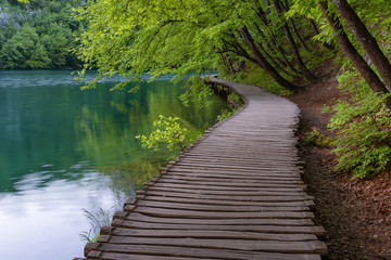 Fototapeta na wymiar Beautiful view of waterfalls with turquoise water and wooden pathway through over water. Plitvice Lakes National Park, Croatia. Famous attraction, summer landscape.