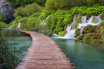 Beautiful view of waterfalls with turquoise water and wooden pathway through over water. Plitvice Lakes National Park, Croatia. Famous attraction, summer landscape.