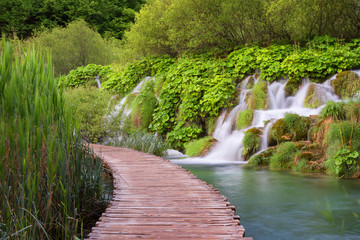 Beautiful view of waterfalls with turquoise water and wooden pathway through over water. Plitvice Lakes National Park, Croatia. Famous attraction, summer landscape.