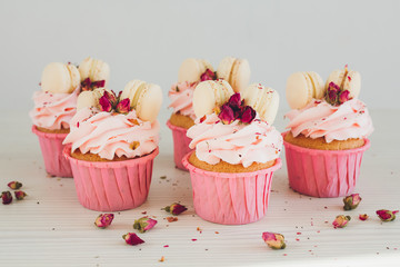 Cupcakes with pink cream, macaroons and roses