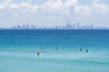 Surfers sit on their boards in front of the Surfer's Paradise skyline, Gold Coast, Queensland,...
