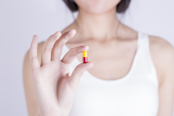 Fototapeta na wymiar Closeup shot of a woman showing yellow capsule pill. Female hand holding a medicine. Shallow depth of field with focus on yellow and red capsule pill. 
