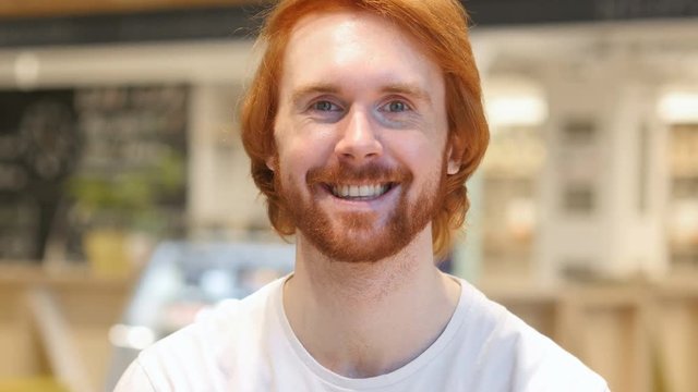 Portrait of Smiling Redhead Beard Man Looking at Camera in Cafe