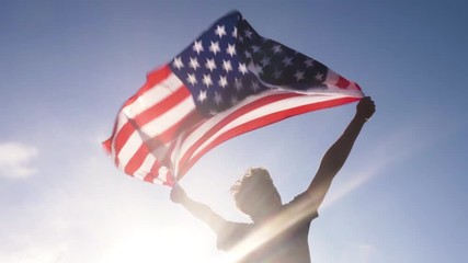 Young man holding american national flag to the sky with two hands at the beach at sunset usa - Powered by Adobe