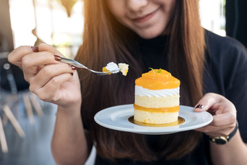 Closeup image of a beautiful Asian woman holding and eating an orange cake in modern cafe