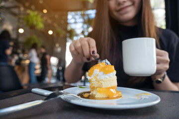 Closeup image of a beautiful Asian woman eating an orange cake while drinking coffee in modern cafe